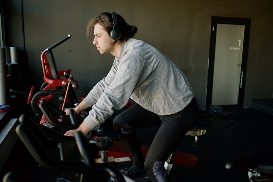 Adult man exercising on a stationary bike indoors, focusing on his workout with headphones.